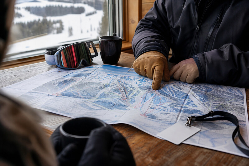 A skier reviewing a folded trail map beside goggles and coffee before skiing Crested Butte