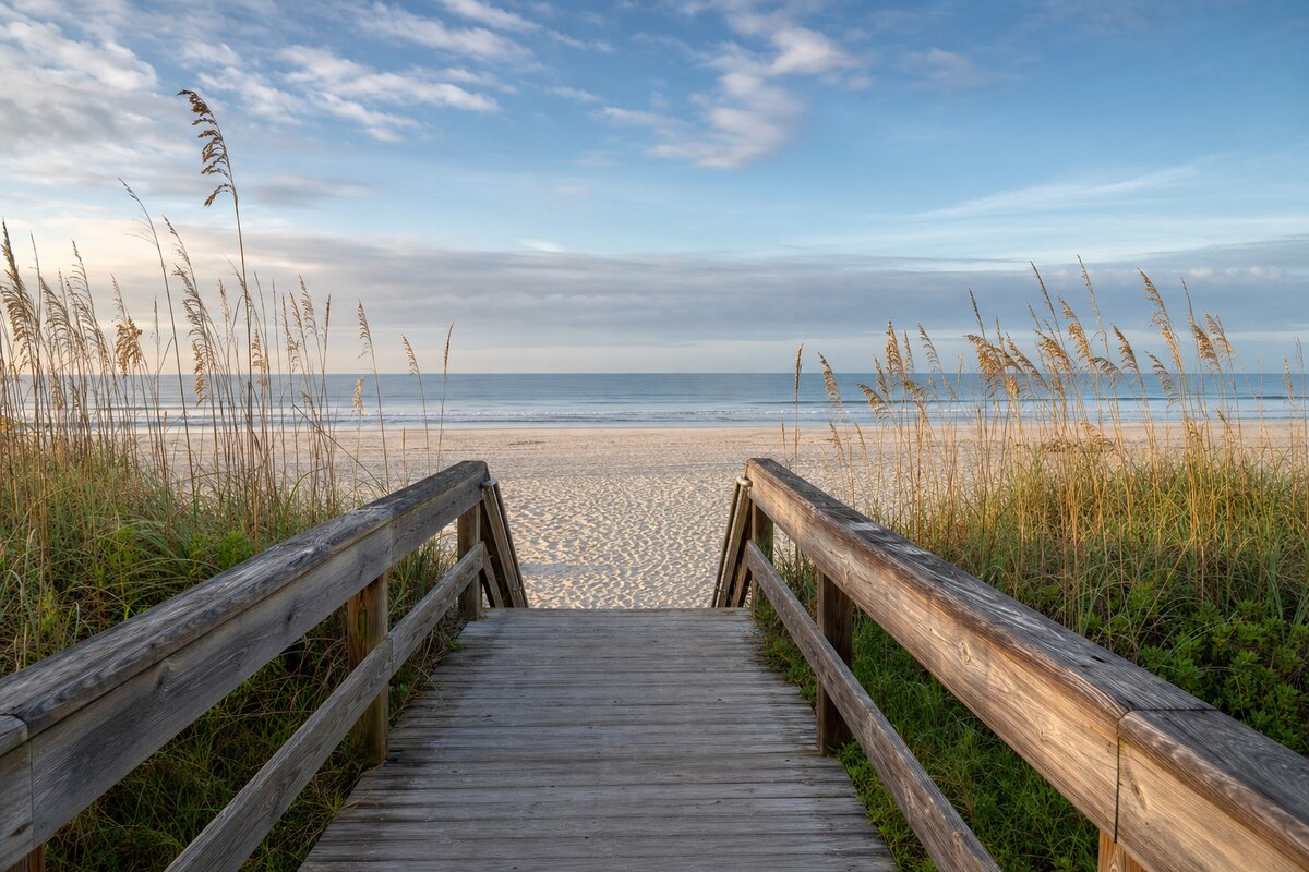 Wooden public beach-access boardwalk through sea oats toward a wide Atlantic beach