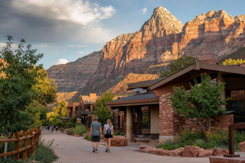 Pedestrians walking through a low-rise Springdale streetscape beneath Zion's sandstone cliffs