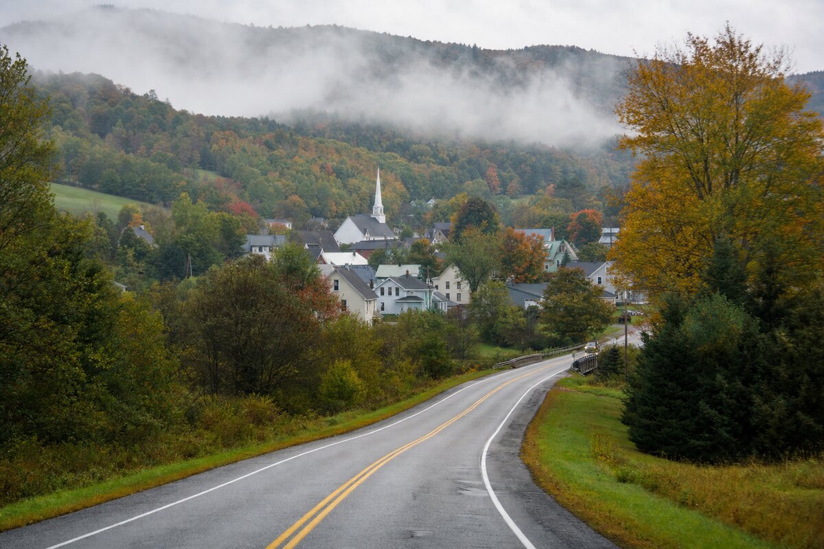 Wet Vermont road approaching a village below a forested ridge
