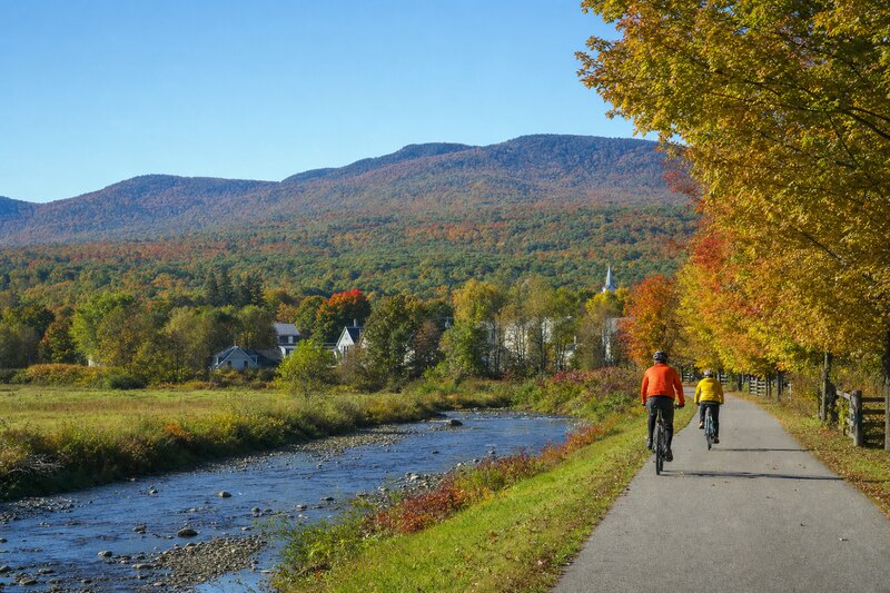 Cyclists on a paved riverside path below the Green Mountains